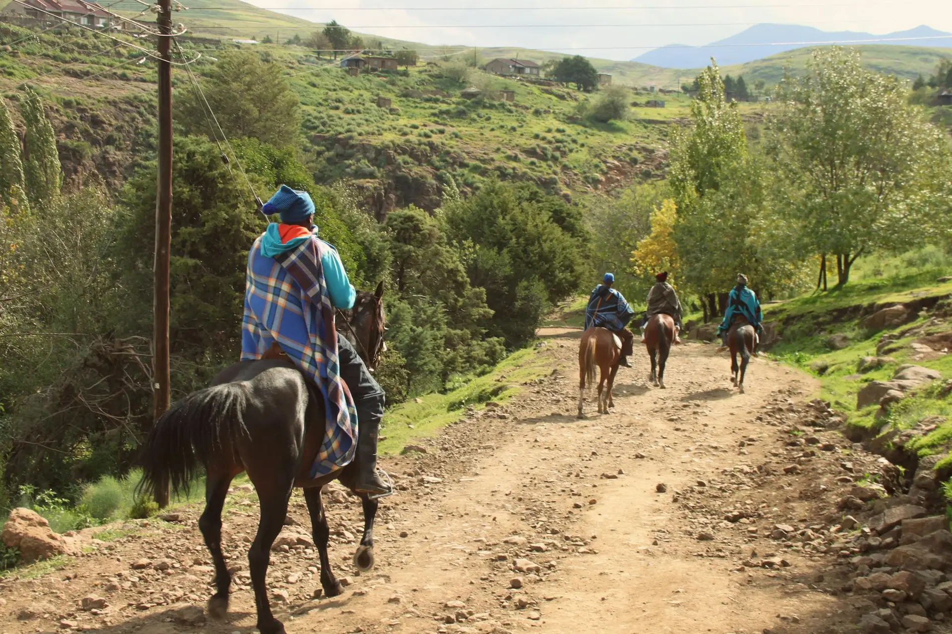 Horse riders on a scenic dirt trail in Semonkong, Maseru, Lesotho, surrounded by lush greenery.