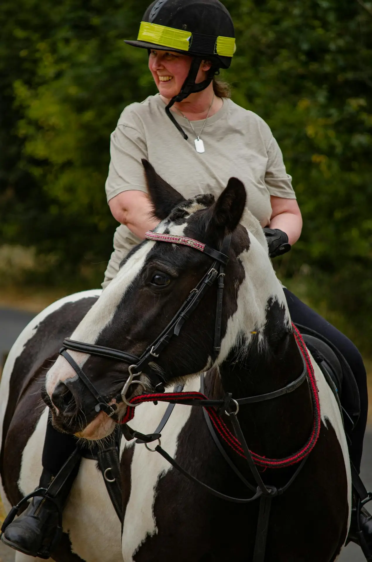 Smiling woman enjoying horseback riding on a black and white horse in an outdoor setting.